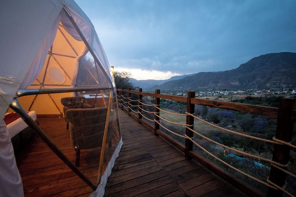 A wooden deck with a rope barrier, a chair, and a transparent tent structure.