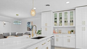 A modern kitchen with white cabinetry, gold handles, and a marble countertop.