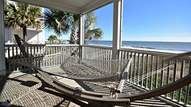 A hammock on a wooden deck with a view of the ocean.