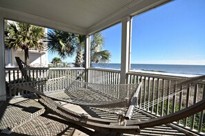 A hammock on a wooden deck with a view of the ocean.