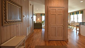 A hallway with wooden walls, a bench, a door, and a dining area with chairs and a table.
