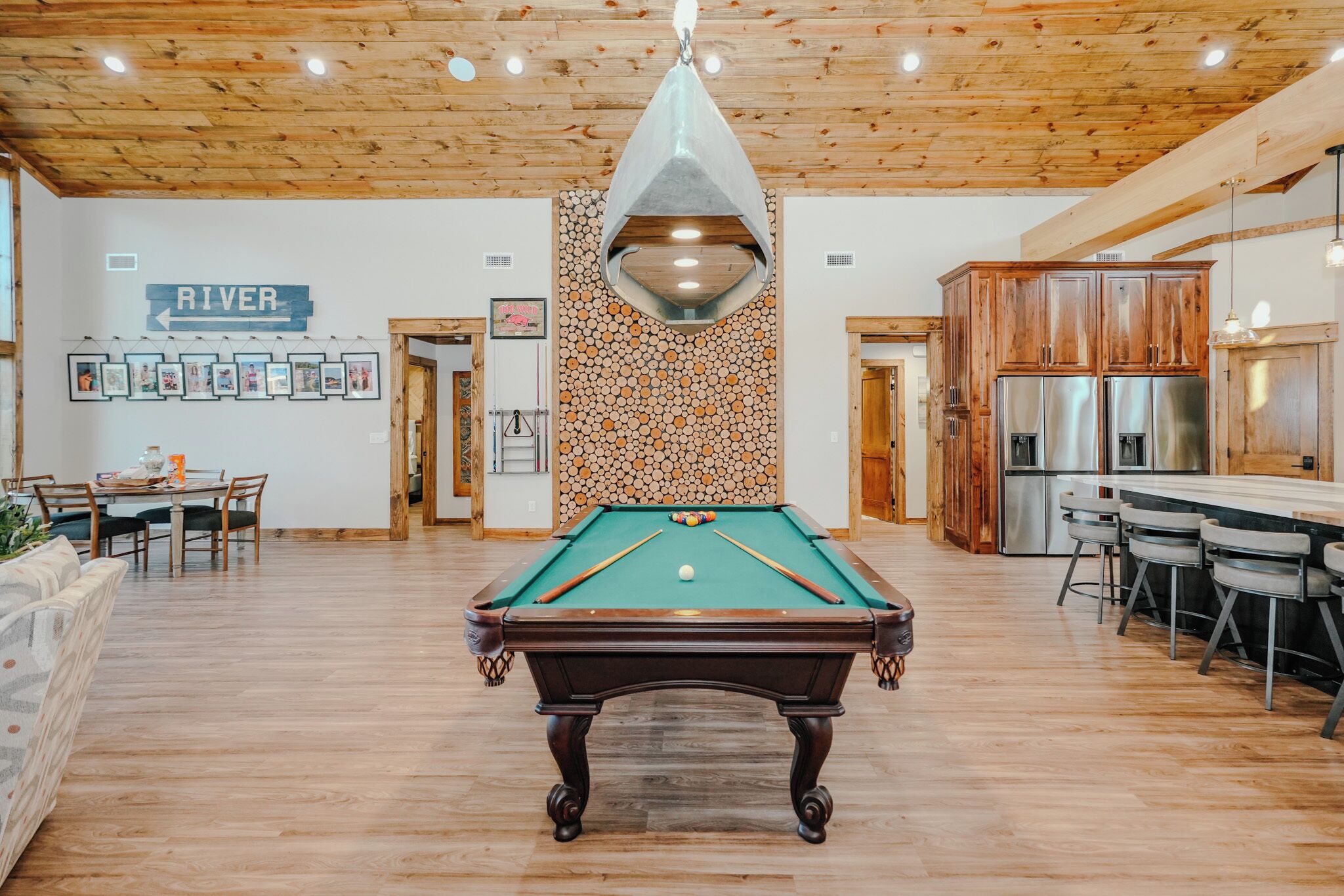 A pool table in a room with wooden floors and a wooden ceiling. There is a sign on the wall that says "RIVER".