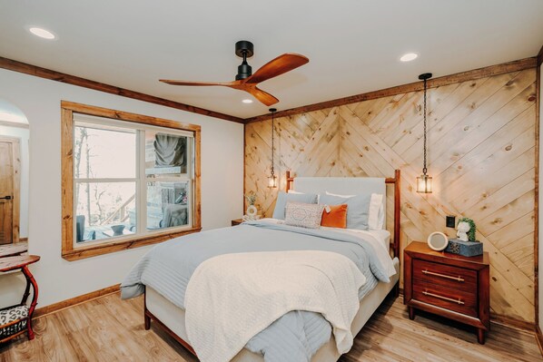 A bedroom with a bed, wooden walls, a window, a ceiling fan, and a bedside table with a lamp. - Riverfront Lodge•Private River Access•Outdoor Living•Lake Greeson + Diamond Mine (Murfreesboro)