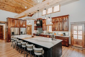 A spacious kitchen with wooden cabinets, a large island with bar stools, pendant lighting, and a farmhouse-style ceiling. - Riverfront Lodge•Private River Access•Outdoor Living•Lake Greeson + Diamond Mine (Murfreesboro)