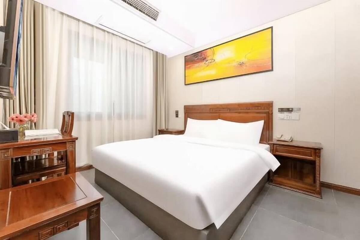 Une chambre d’hôtel avec un grand lit, des tables de chevet en bois, un bureau et un tableau au mur.