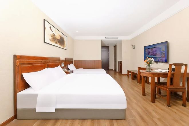 Een hotelkamer met een groot bed, een bureau met stoel, een televisie en een schilderij aan de muur.