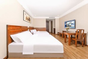 Habitación de hotel con una cama grande, cabecera de madera, escritorio con silla y televisor en la pared.