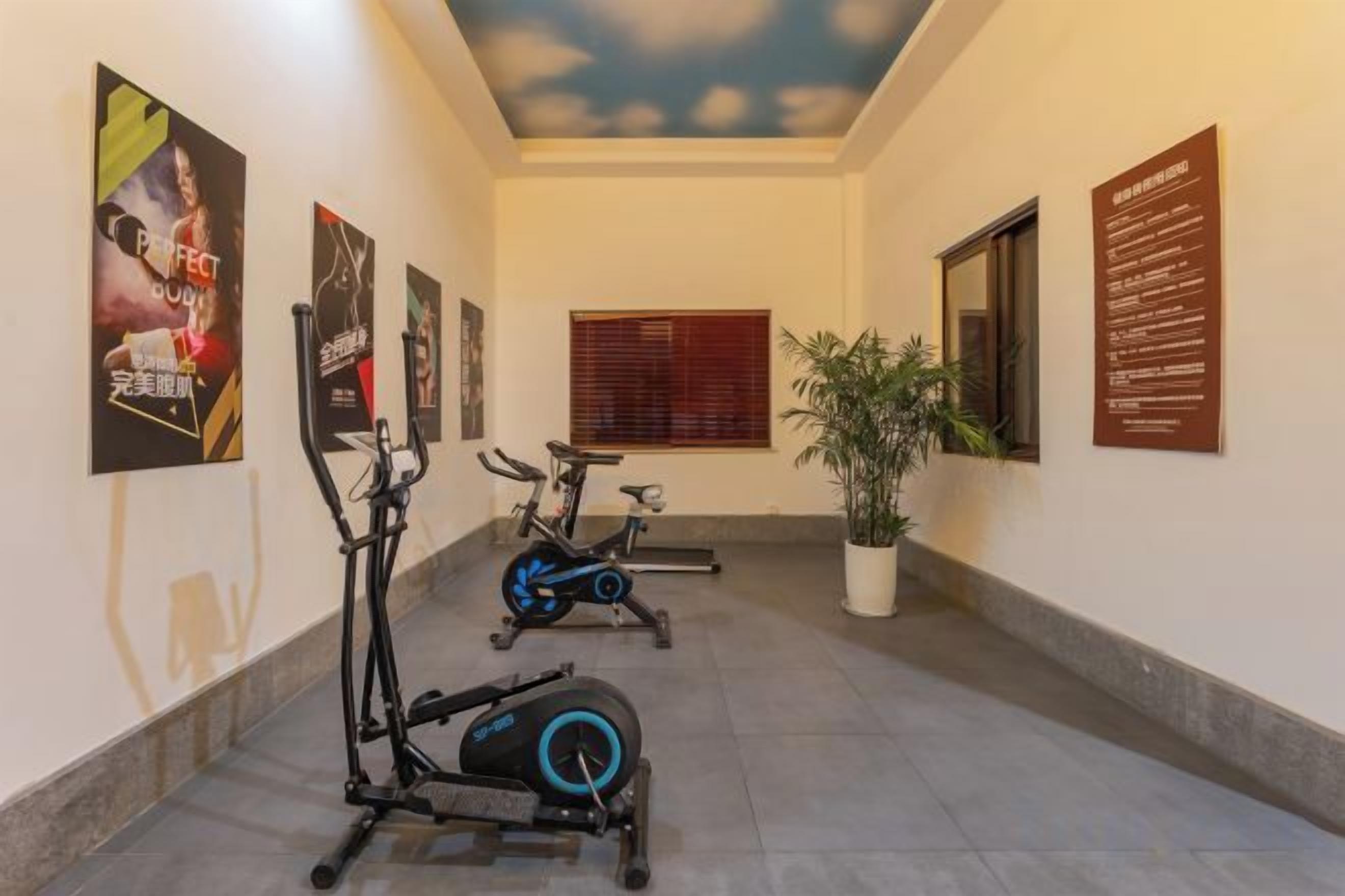 Un pasillo con bicicletas estáticas, una planta en maceta y carteles informativos en las paredes.