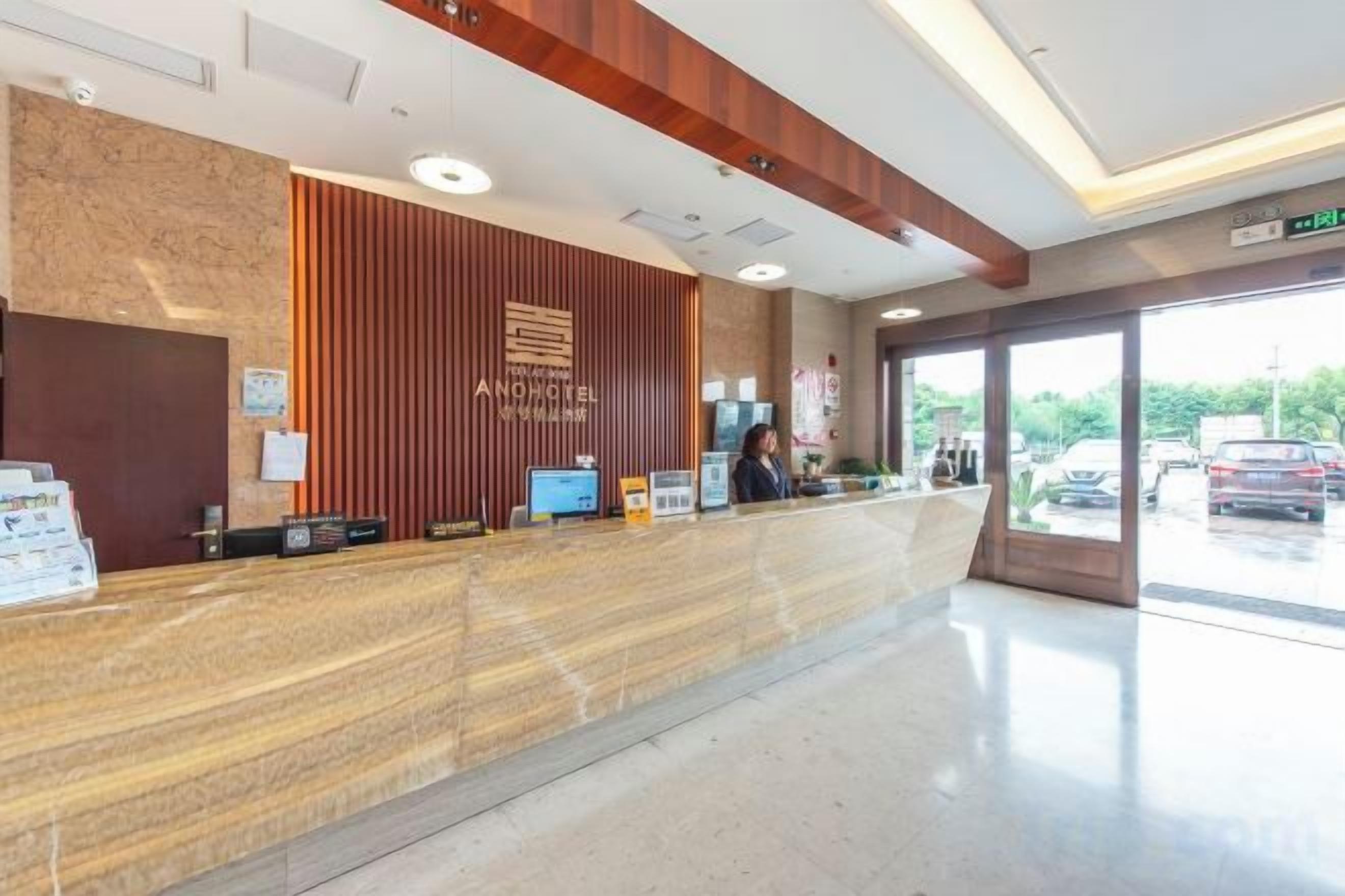A hotel reception area with a marble counter, a wooden accent wall, and a view of the parking lot through large windows.