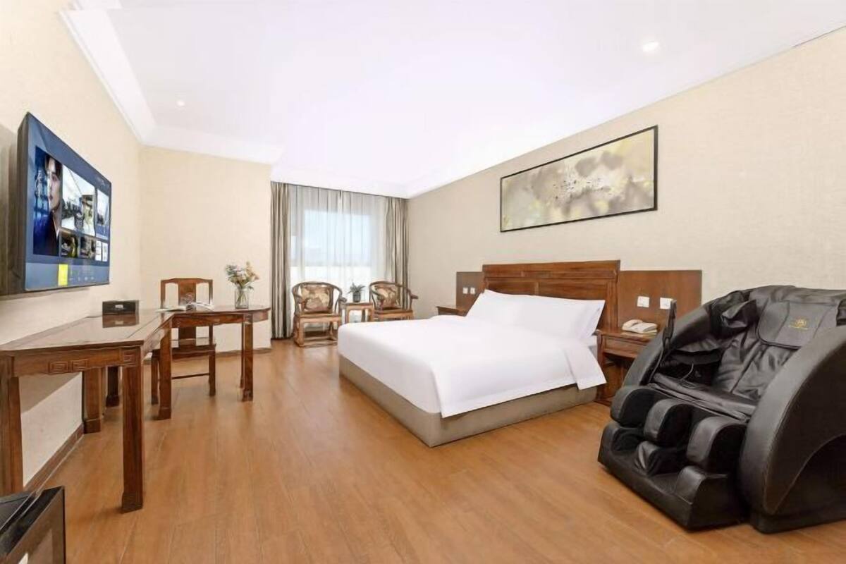 Une chambre d’hôtel équipée d’un lit, d’un fauteuil massant, d’un bureau, de chaises et d’une télévision.