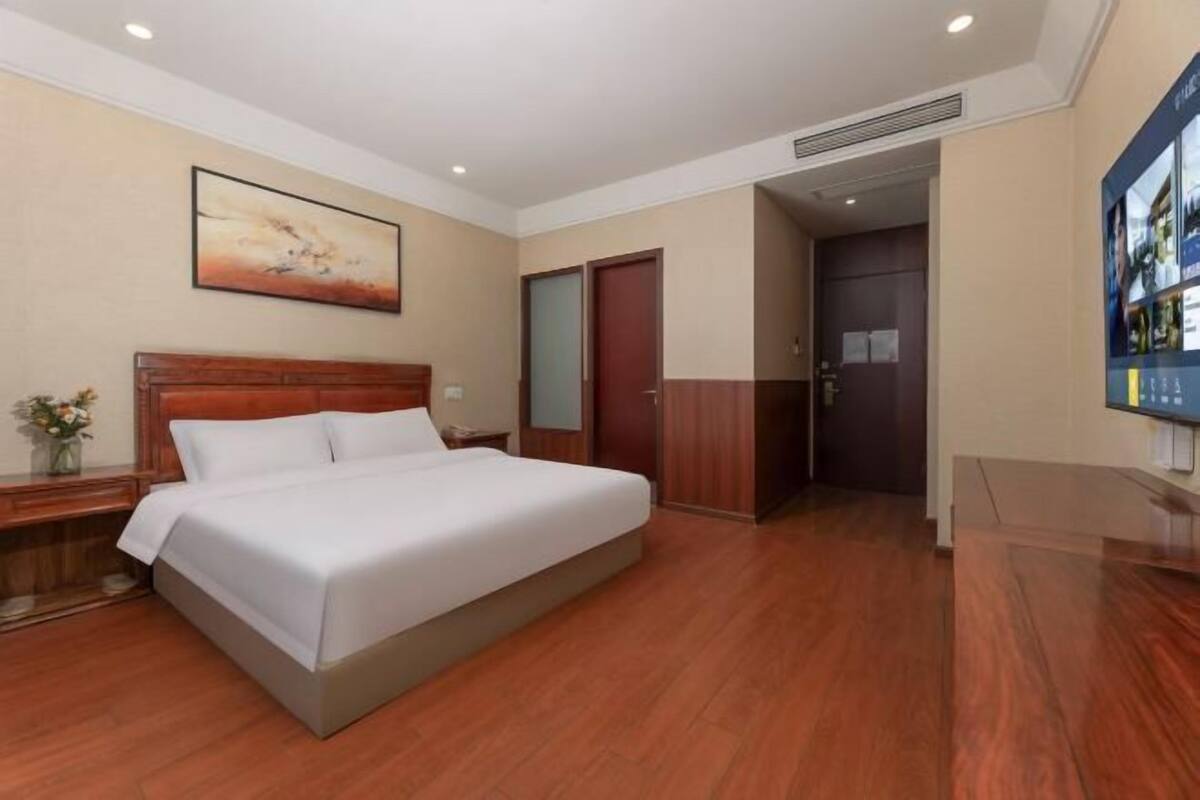 Une chambre d’hôtel avec un lit, une table de chevet, un tableau, une porte et un téléviseur fixé au mur.