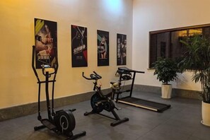 Un gimnasio con bicicletas estáticas, cinta de correr y equipo de ejercicio. Hay carteles en la pared y una planta en maceta.