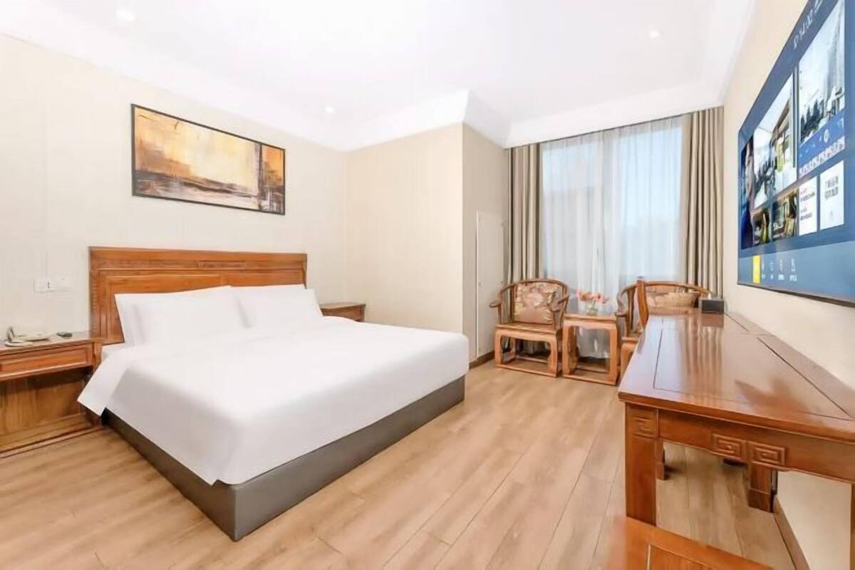 Une chambre d’hôtel avec un lit, un bureau, une chaise, une table de chevet et un tableau au mur.
