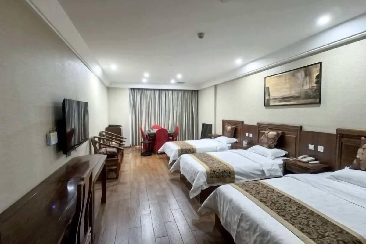Une chambre d’hôtel avec trois lits, une télévision, un bureau et un coin repas.