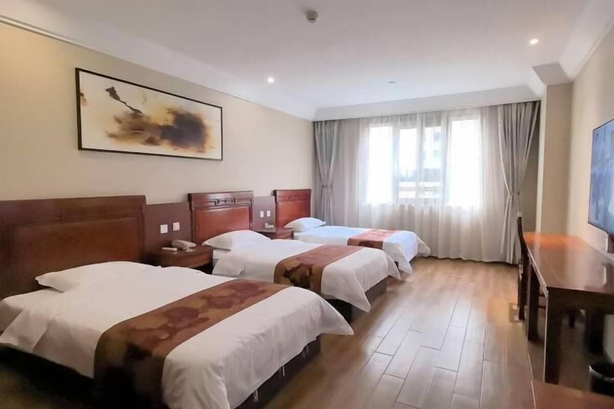 Une chambre d’hôtel avec trois lits, un plancher en bois, un bureau et un grand tableau accroché au mur.