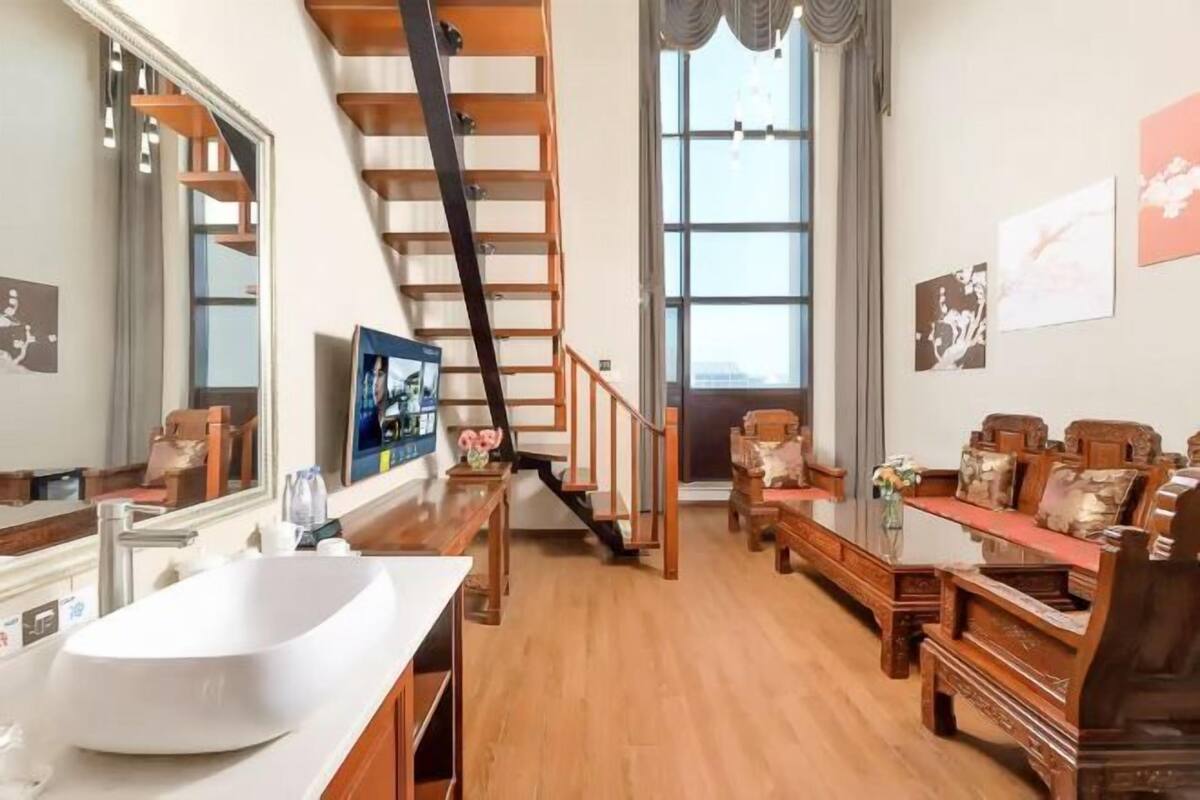 Un vaste espace de vie agrémenté d’un escalier en bois, d’une grande fenêtre et d’un ensemble de canapés.