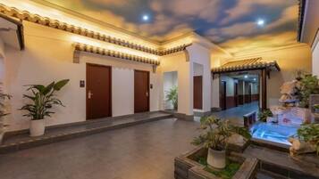 A hotel corridor with a ceiling mural, potted plants, and a water feature.