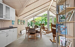 Uma cozinha moderna com armários de madeira, uma área de refeições com mesa e cadeiras, e uma estante cheia de livros.