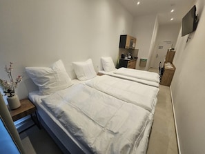 Une chambre d’hôtel avec deux lits, un petit bureau, un téléviseur fixé au mur et un coin cuisine.