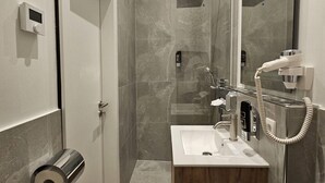 A modern bathroom with a shower, a sink, and a toilet. There are toilet paper rolls and a towel rack visible.