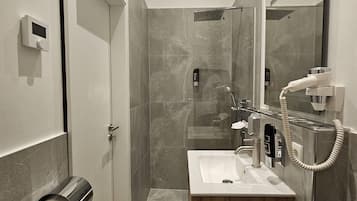 Ein modernes Badezimmer mit Dusche, Waschbecken und Toilette. Toilettenpapierrollen und ein Handtuchhalter sind sichtbar.
