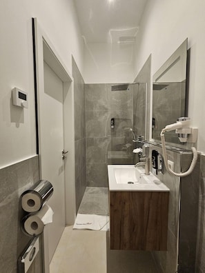 Une salle de bain moderne équipée d’une douche, d’un lavabo et de toilettes. On peut voir des rouleaux de papier toilette et un porte-serviettes.