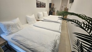A hotel room with three beds, a large potted plant, and a cityscape artwork on the wall. - Aparthotel Rahl (Hamburg)
