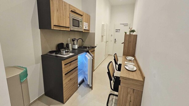 A compact kitchen with wooden cabinets, a microwave, and a built-in oven. There is a small dining area with a table set for two. - Aparthotel Rahl (Hamburg)