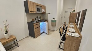A compact kitchen with modern appliances, a dining area with a wooden table set for four, and a small side table with a vase. - Aparthotel Rahl (Hamburg)