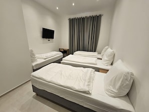 Une chambre d’hôtel avec deux lits simples, un bureau, une chaise, un téléviseur à écran plat fixé au mur et une fenêtre avec des rideaux gris.