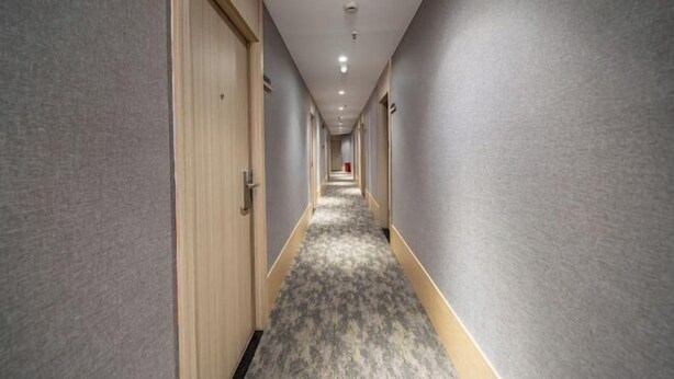 A long, narrow hotel corridor with carpeted floors and wooden doors on one side.