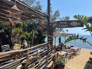 A beachside restaurant with outdoor seating, wooden tables, and chairs, and a sign reading 'Marius A La Plage.'