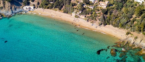 An aerial view of a coastal area with a sandy beach, clear turquoise waters, and residential buildings.