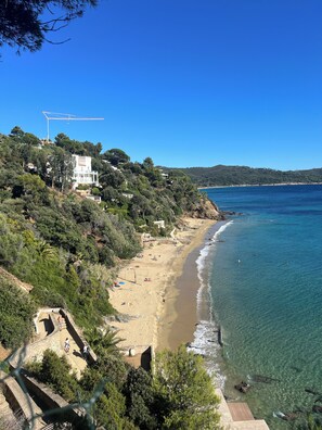 A coastal landscape with a sandy beach, clear blue waters, and a construction crane in the distance.