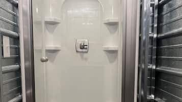 A walk-in shower with a glass door, a control panel, and a showerhead.