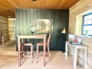 Un intérieur en bois comprenant une table à manger et des chaises, une lampe fixée au mur et une fenêtre donnant sur des arbres.