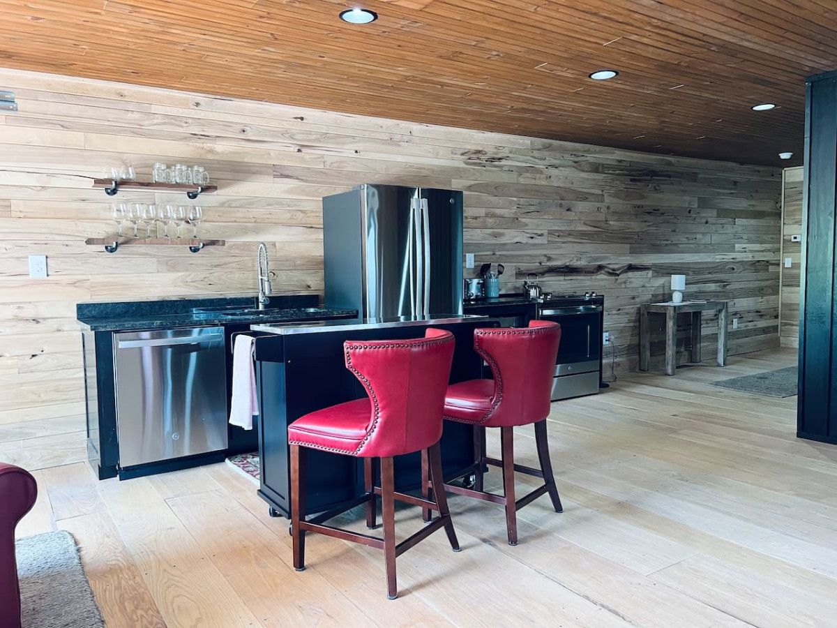 Una cocina moderna con una pared de madera, electrodomésticos de acero inoxidable y taburetes rojos.