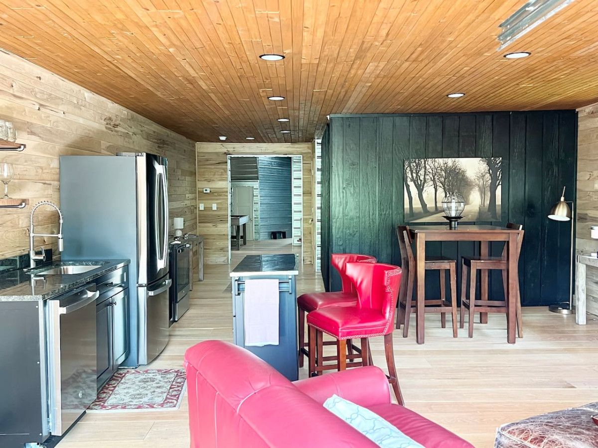 A modern kitchen with stainless steel appliances, a dining area with wooden furniture, and a red sofa.
