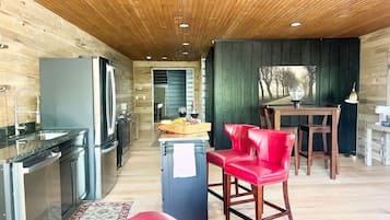 Una cocina moderna con electrodomésticos de acero inoxidable, techo de madera y un comedor con una silla roja.