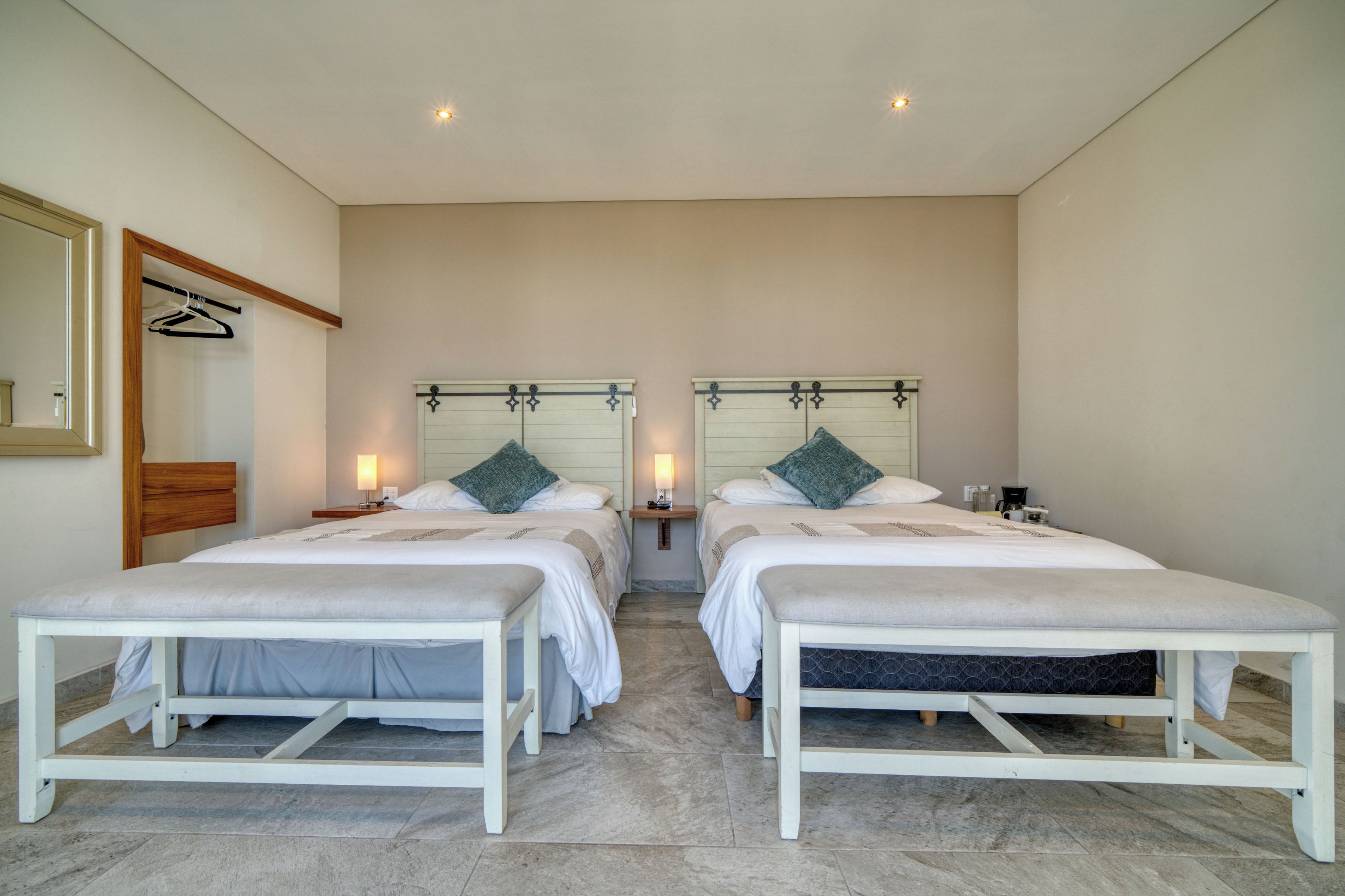 Habitación de hotel con dos camas, cabecera de madera, un espejo y una mesita de noche con lámpara.
