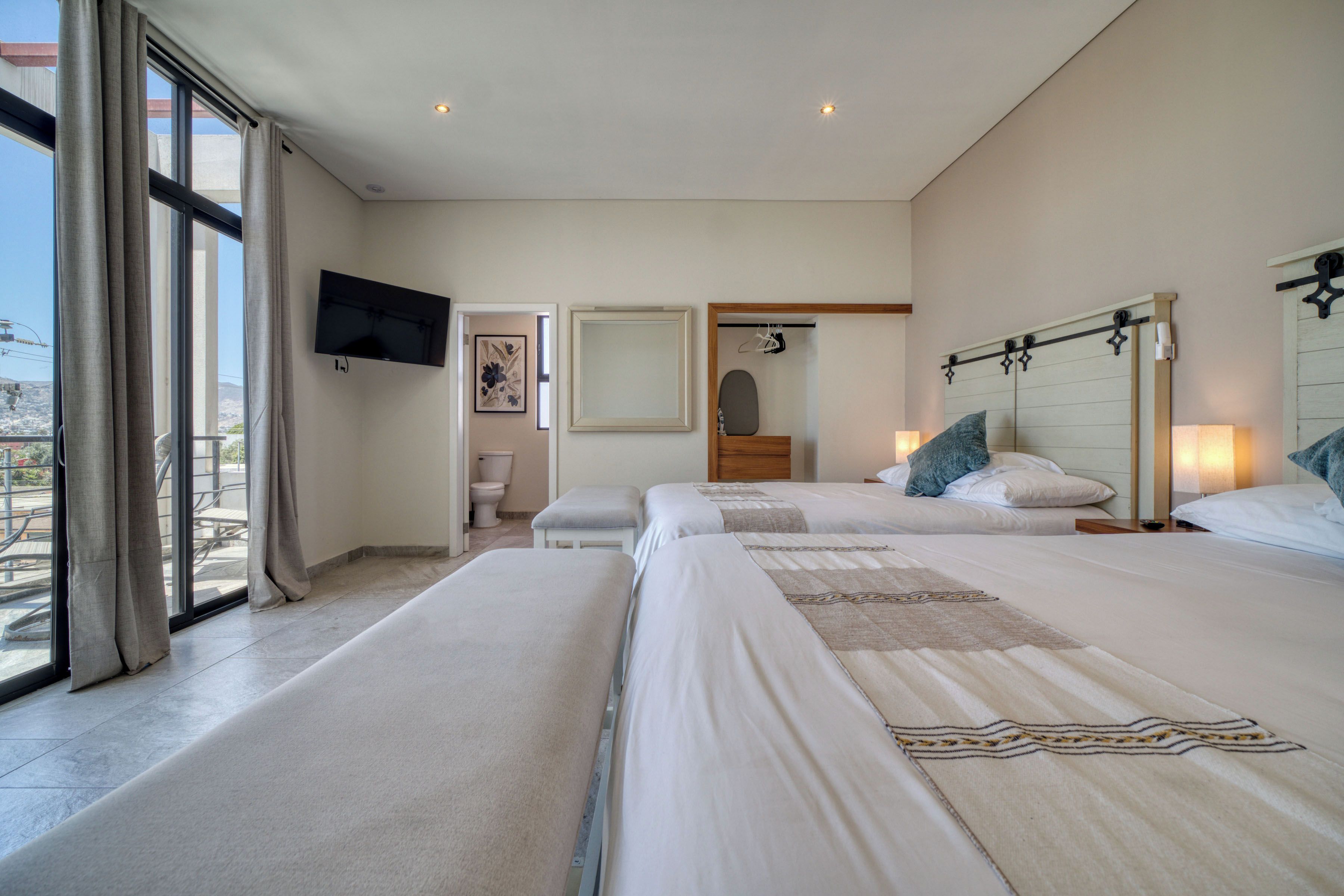 A hotel room with two beds, a television, a bathroom, and a balcony.