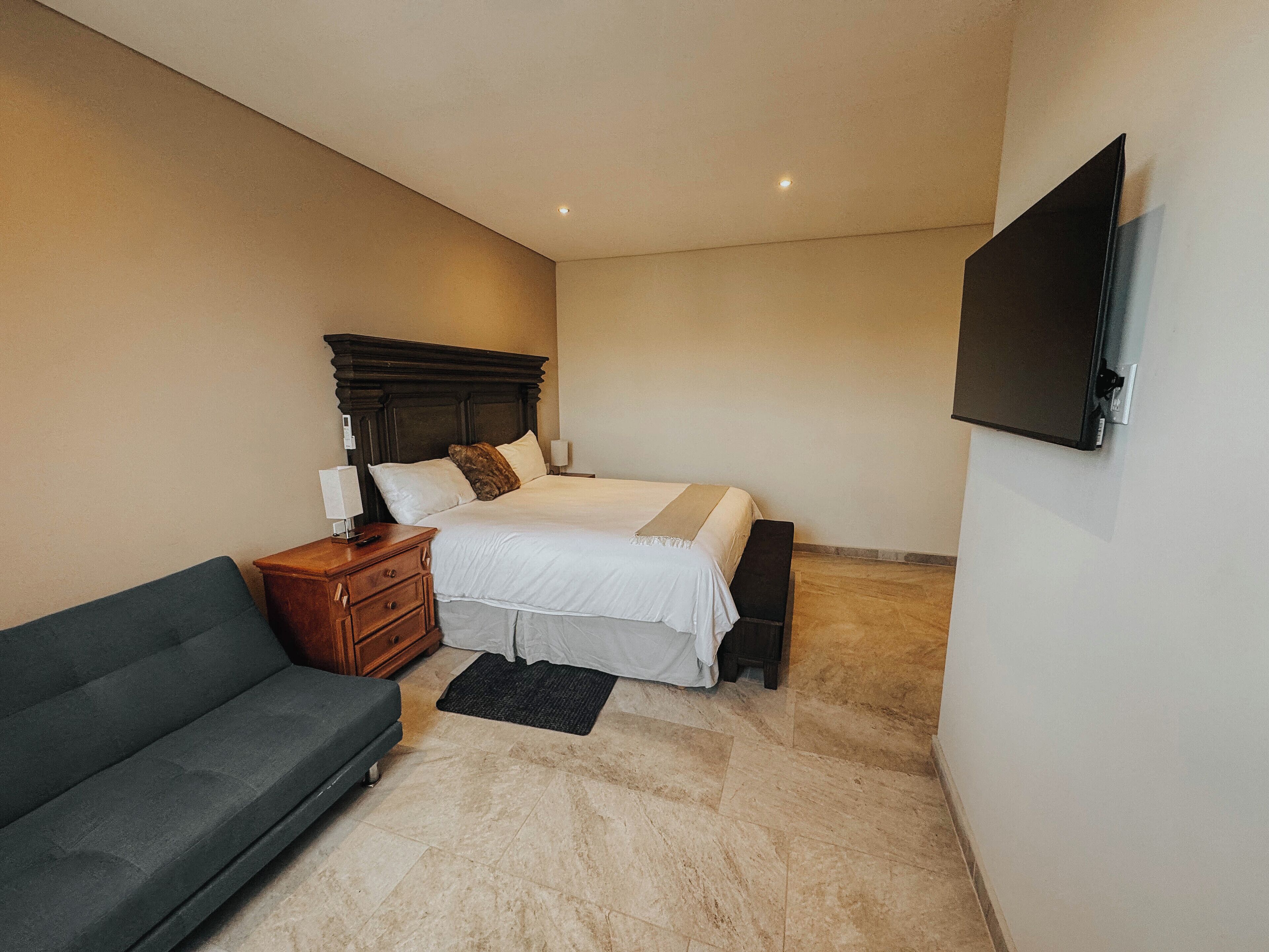 A bedroom with a bed, bedside table, lamp, and a flat-screen TV mounted on the wall.