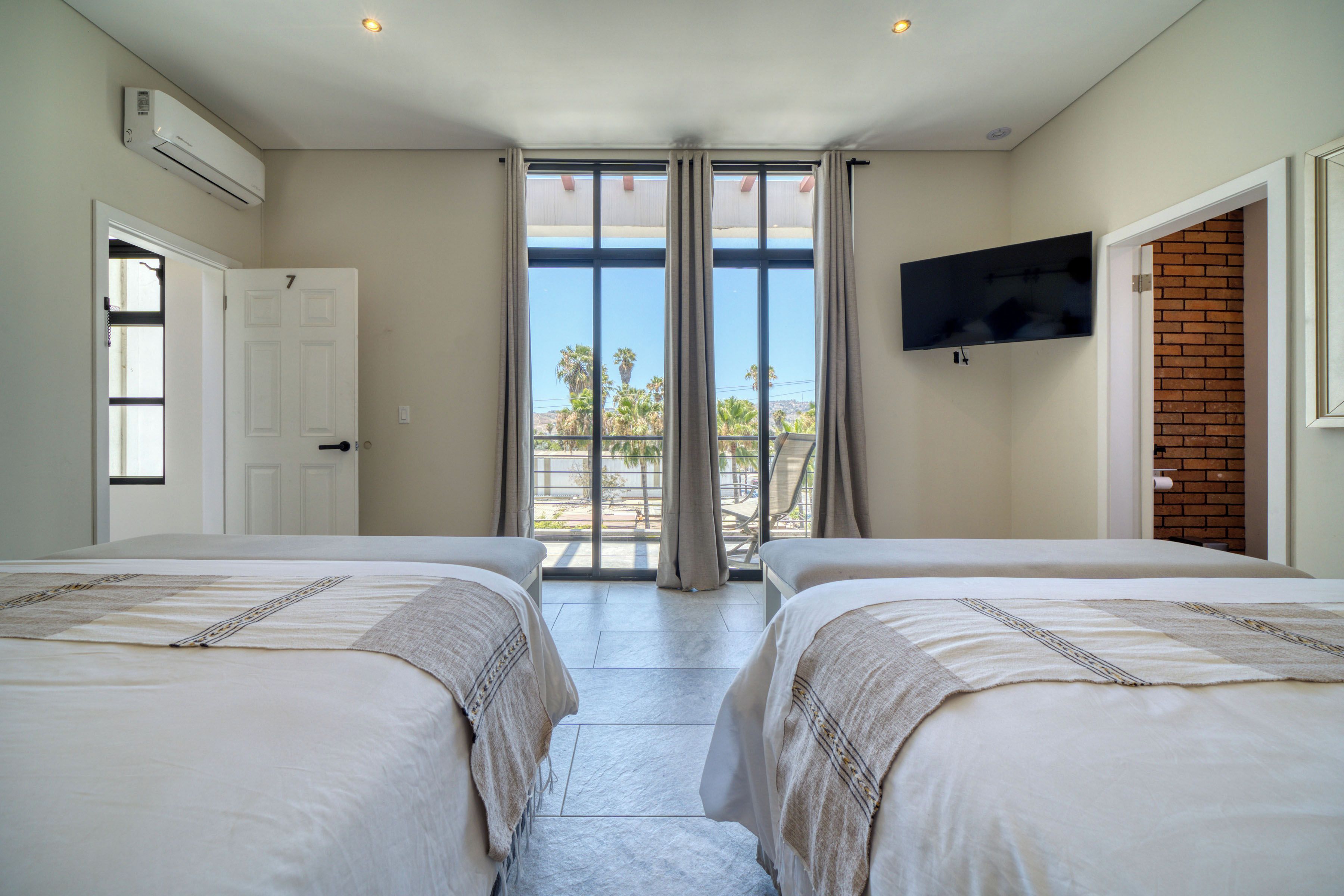 A hotel room with two beds, a TV, and a balcony with a view.