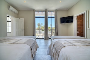 A hotel room with two beds, a TV, and a balcony with a view. - Suites Lassa (Ensenada)