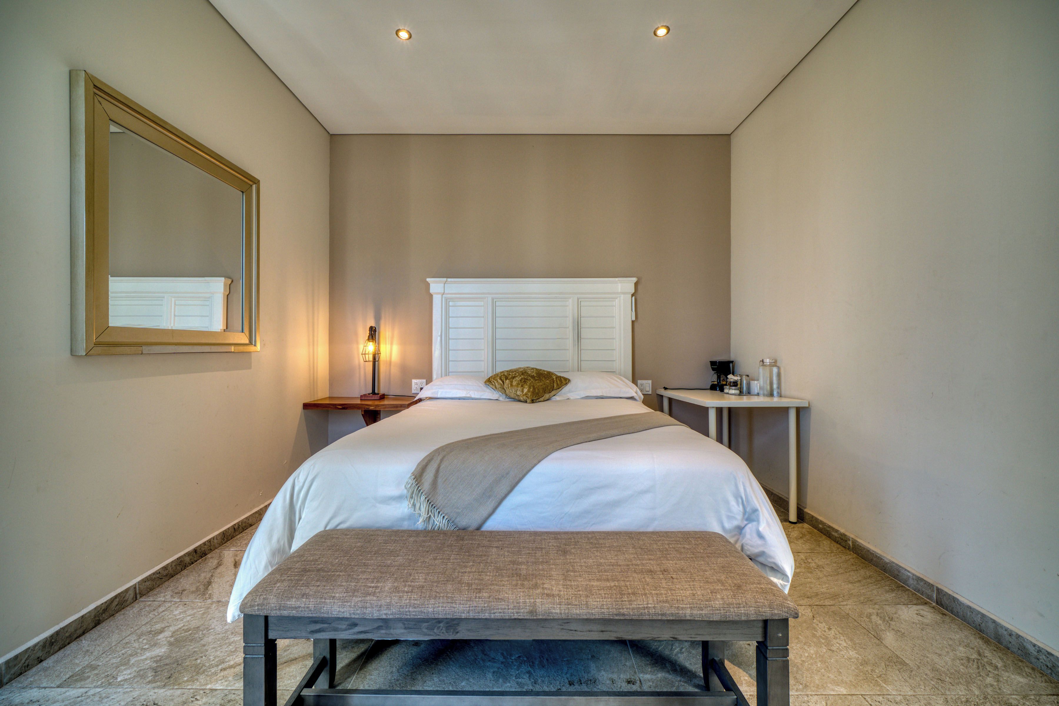 A hotel room with a large bed, a bedside table with a lamp, a bench, and a mirror on the wall.