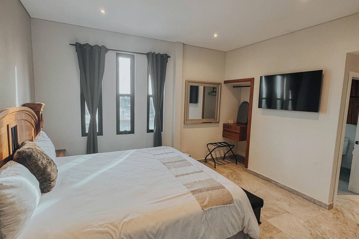 A modern bedroom with a large bed, a flat-screen TV, a mirror, and a window with curtains.