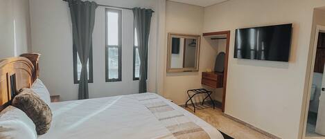 A modern bedroom with a large bed, a flat-screen TV, a mirror, and a window with curtains.