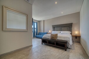 Un dormitorio con una cama grande, un banco, un sofá azul y un aplique de pared.