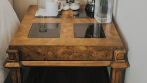 A wooden nightstand with a coffee maker, a glass pitcher, and a mug. - Suites Lassa (Ensenada)
