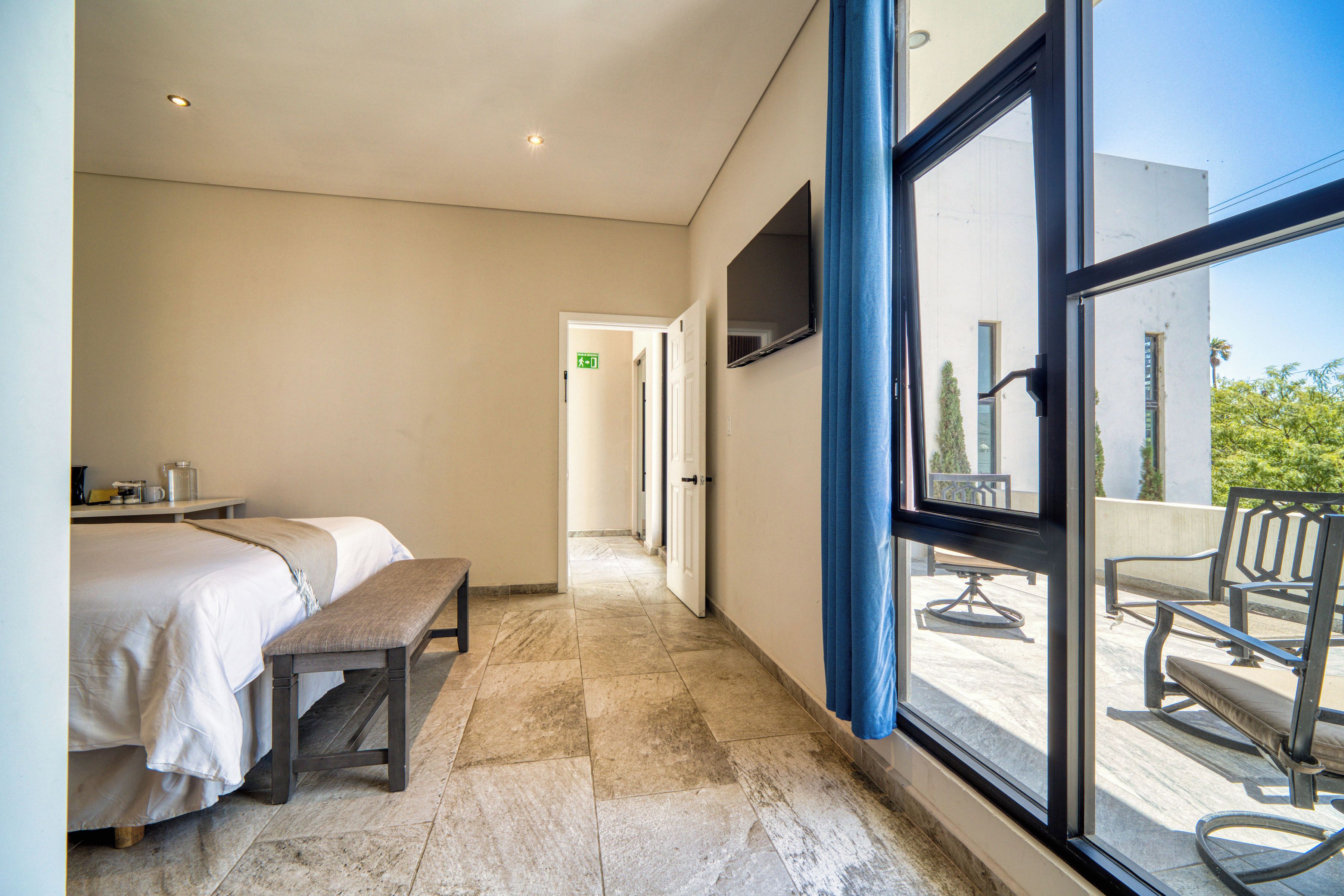 A hotel room with a bed, bench, and a view of the outdoor area through large windows.